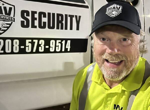 A man in a security vest and hat standing next to a van.