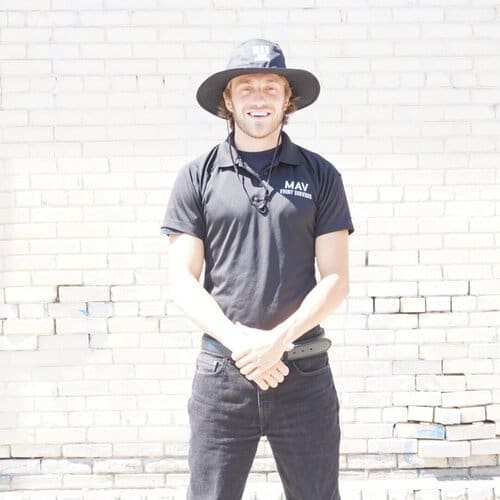 A man in black shirt and hat standing next to brick wall.